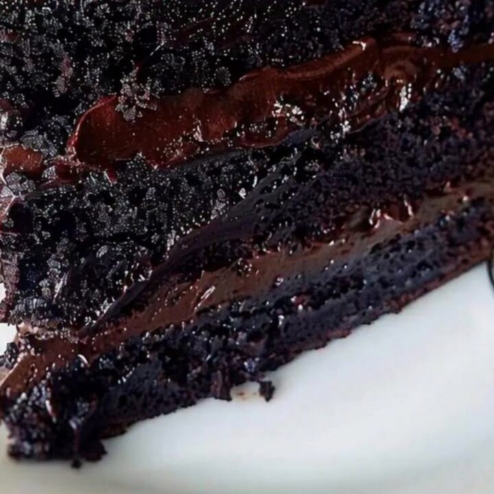 Une part de gâteau au chocolat brillant avec une ganache onctueuse sur une assiette blanche.