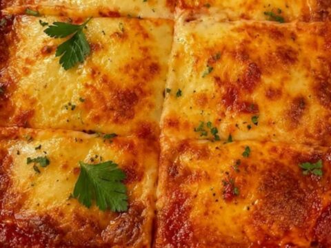A close-up of a portion of baked lasagna with melted mozzarella being lifted by a spatula.