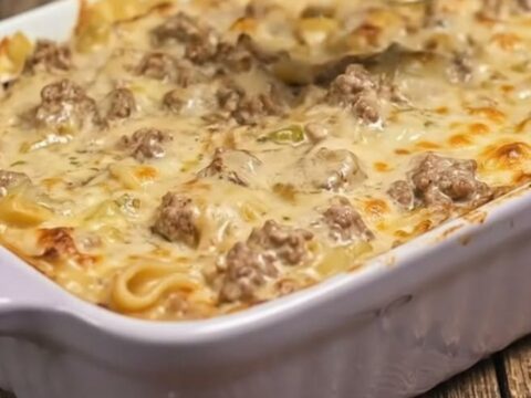 A close-up of a serving of creamy beef stroganoff bake in a fluted dish with melted cheese pulls.