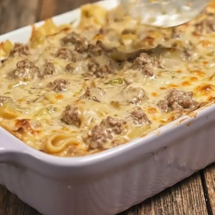 A close-up of a serving of creamy beef stroganoff bake in a fluted dish with melted cheese pulls.
