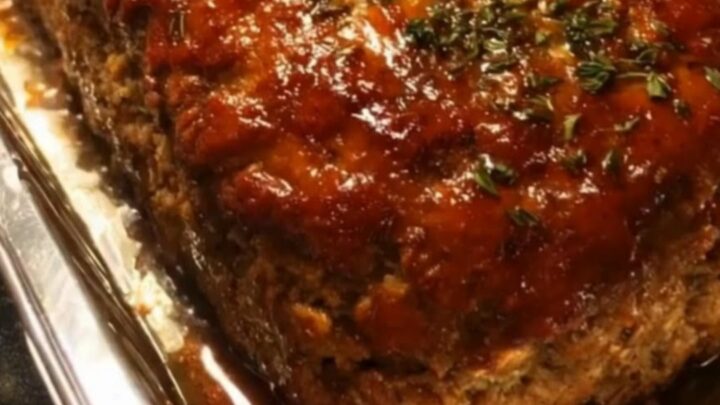 A glistening glazed meatloaf sitting in a foil pan on a kitchen counter.