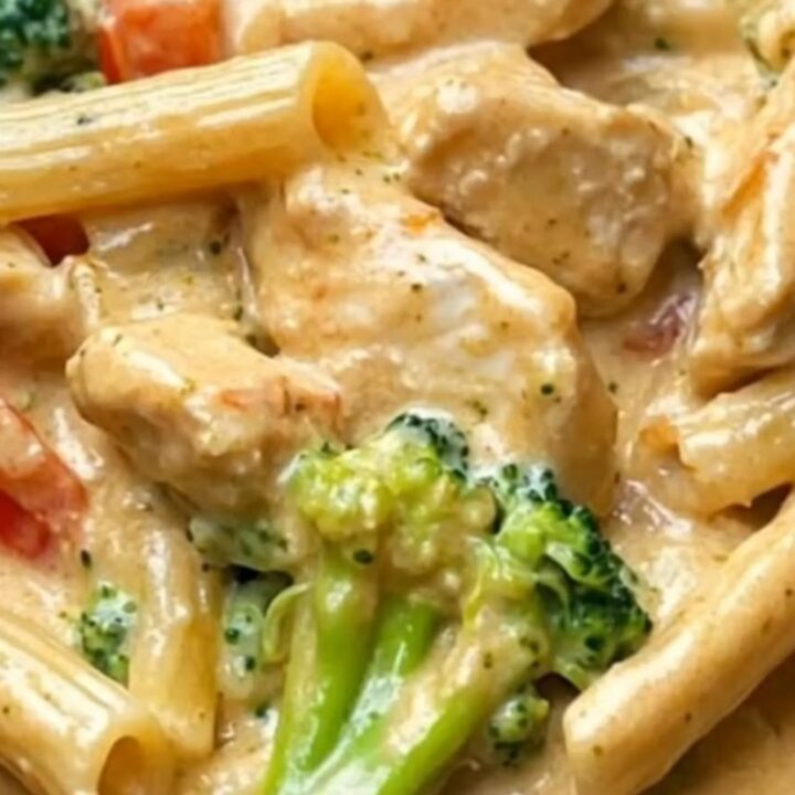 A close-up of a creamy chicken and broccoli penne pasta dish in a skillet with a rich cheese pull.