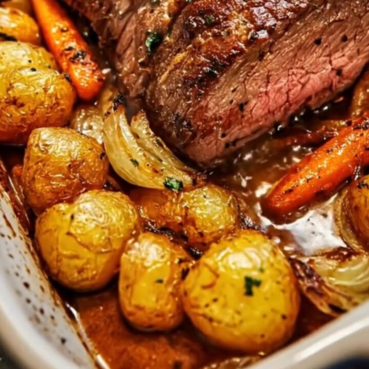 A ceramic dish filled with a sliced herb-crusted roast beef surrounded by roasted baby potatoes and carrots.