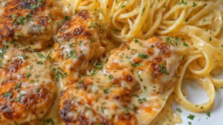 A plate of creamy parmesan fettuccine topped with golden brown chicken bites and fresh herbs.
