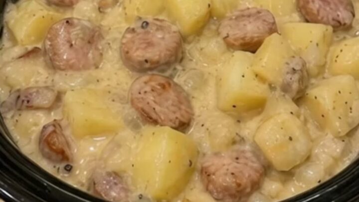 A slow cooker filled with creamy, bubbling swamp potatoes and sliced smoked sausage.
