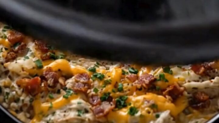 A serving spoon lifting creamy shredded crack chicken with melted cheddar and bacon from a slow cooker.