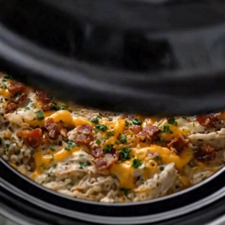 A serving spoon lifting creamy shredded crack chicken with melted cheddar and bacon from a slow cooker.