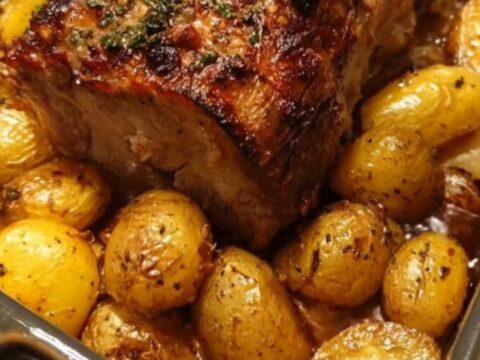A beautifully roasted pork loin with crispy golden baby potatoes in a dark roasting pan, ready to serve.