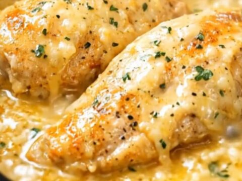 A close-up of a juicy chicken breast covered in a creamy, herb-flecked parmesan sauce in a slow cooker.