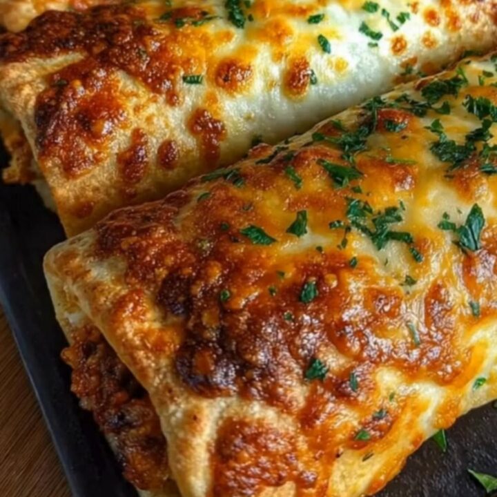 A tray of golden-baked taco sticks garnished with parsley flakes on a dark baking sheet.