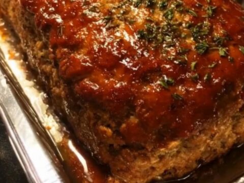 A perfectly glazed and caramelized meatloaf sitting in a metal loaf pan on a kitchen counter.