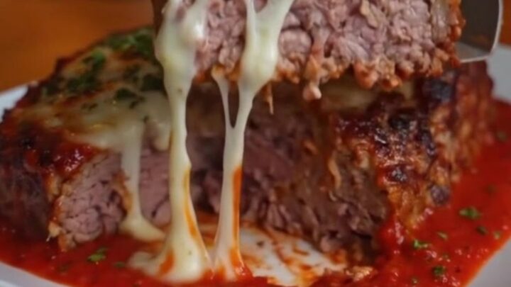 A thick slice of Italian meatloaf on a white plate with melted mozzarella oozing from the center.
