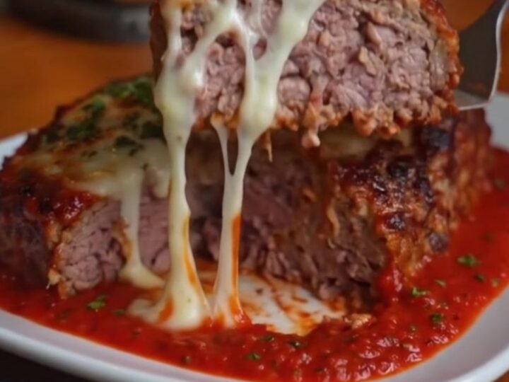 A thick slice of Italian meatloaf on a white plate with melted mozzarella oozing from the center.