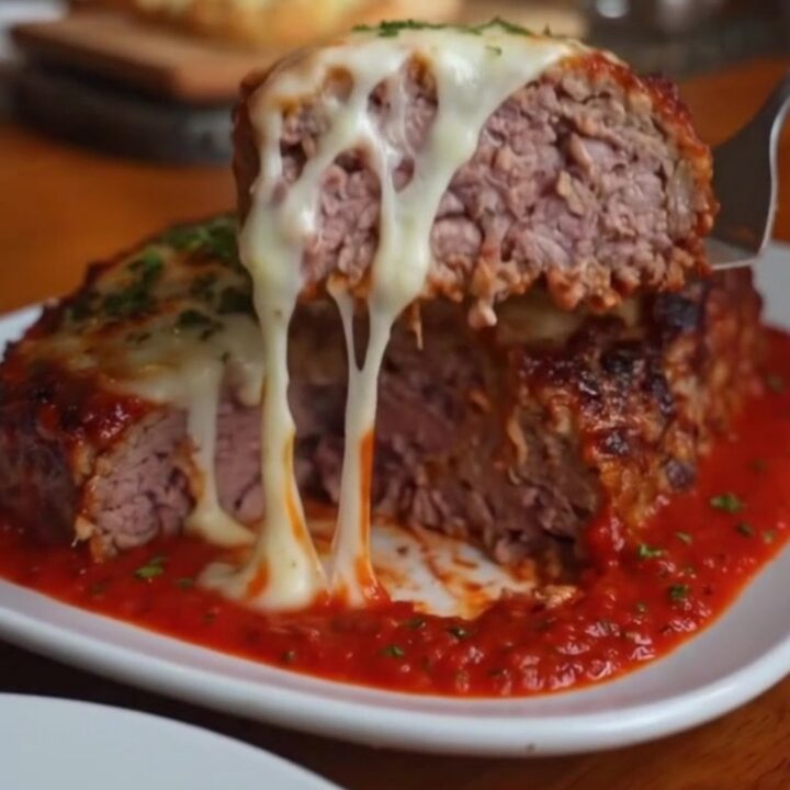 A thick slice of Italian meatloaf on a white plate with melted mozzarella oozing from the center.