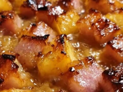 A white baking dish filled with golden, caramelized ham cubes and pineapple pieces covered in a thick brown sugar glaze.
