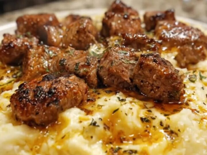A close-up of garlic butter steak bites served over creamy Parmesan mashed potatoes on a white plate.