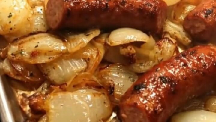 A silver sheet pan filled with golden-brown smoked sausage segments and caramelized onion wedges.