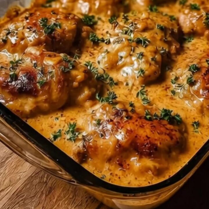 A close-up shot of a spoon lifting a portion of creamy cheesy baked chicken from a glass casserole dish.