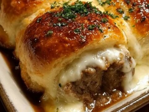 A ceramic baking dish filled with golden brown garlic butter beef rollups, showing melted cheese inside.