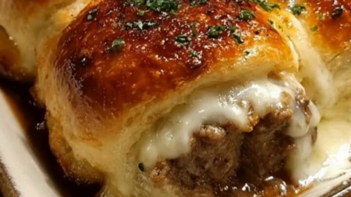 A ceramic baking dish filled with golden brown garlic butter beef rollups, showing melted cheese inside.