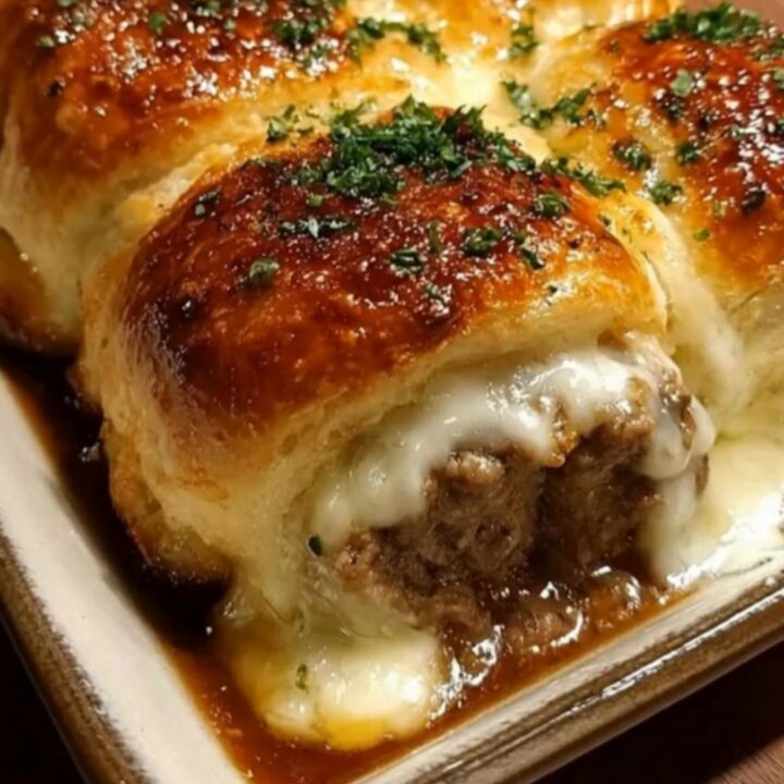 A ceramic baking dish filled with golden brown garlic butter beef rollups, showing melted cheese inside.