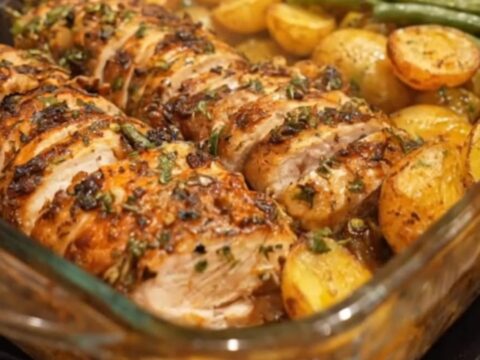 A golden roasted chicken breast sliced next to roasted baby potatoes and tender green beans in a glass dish.