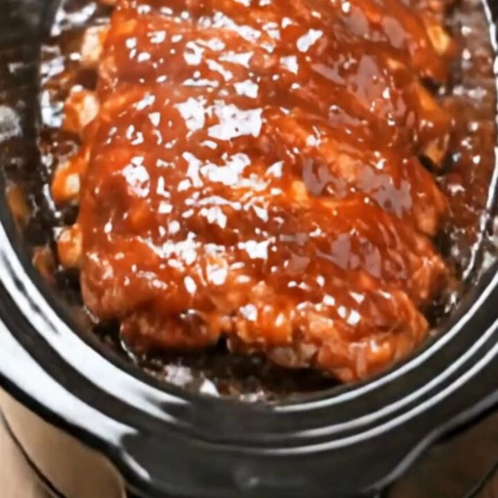 A rack of tender, glazed BBQ ribs sitting on a white plate with sauce dripping down.