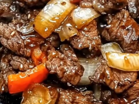 A steaming cast-iron skillet filled with glossy, thin slices of beef, charred green bell peppers, and caramelized onions.