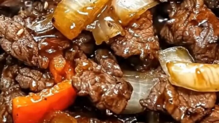 A steaming cast-iron skillet filled with glossy, thin slices of beef, charred green bell peppers, and caramelized onions.