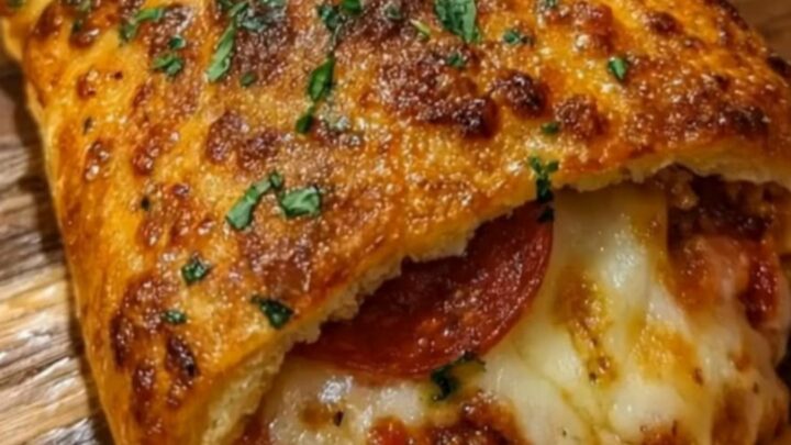 A golden-brown pepperoni pizza stromboli sitting on a rustic wooden board with dipping sauce nearby.