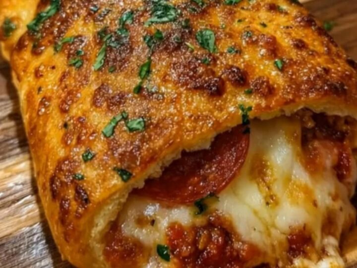 A golden-brown pepperoni pizza stromboli sitting on a rustic wooden board with dipping sauce nearby.