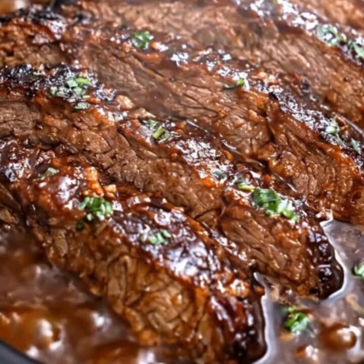 A close-up of tender, glazed beef chuck roast in a slow cooker with a garlic sauce and fresh parsley garnish.
