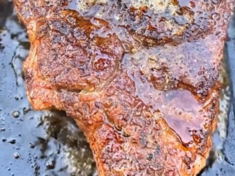 A perfectly seared ribeye steak topped with melting herb garlic butter on a dark cast-iron griddle.
