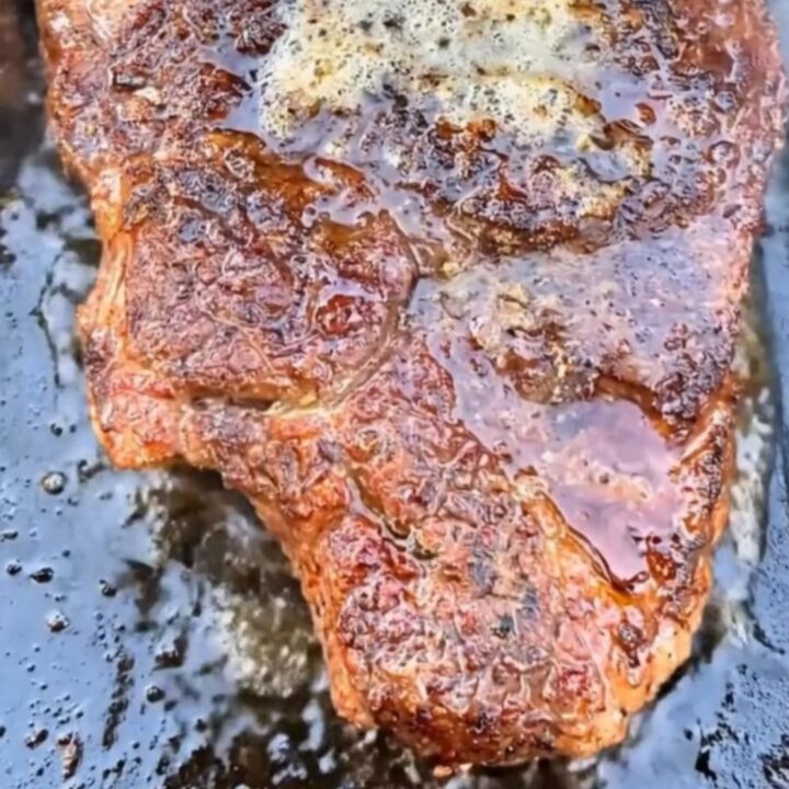 A perfectly seared ribeye steak topped with melting herb garlic butter on a dark cast-iron griddle.