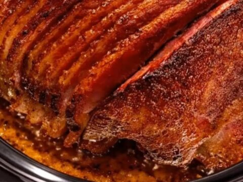 A glistening, brown sugar glazed spiral-sliced ham served on a white platter in a warm kitchen.