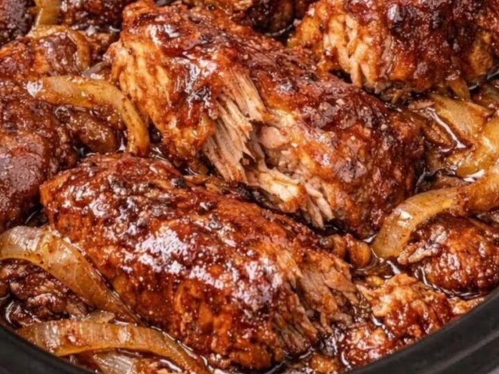 A close-up of tender, saucy country-style ribs in a slow cooker with caramelized onions.
