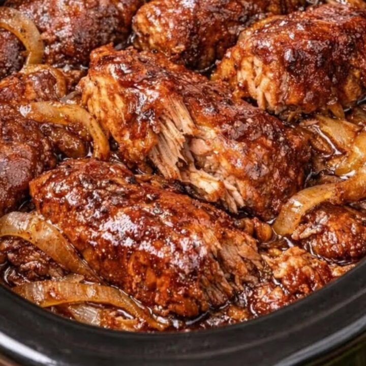 A close-up of tender, saucy country-style ribs in a slow cooker with caramelized onions.