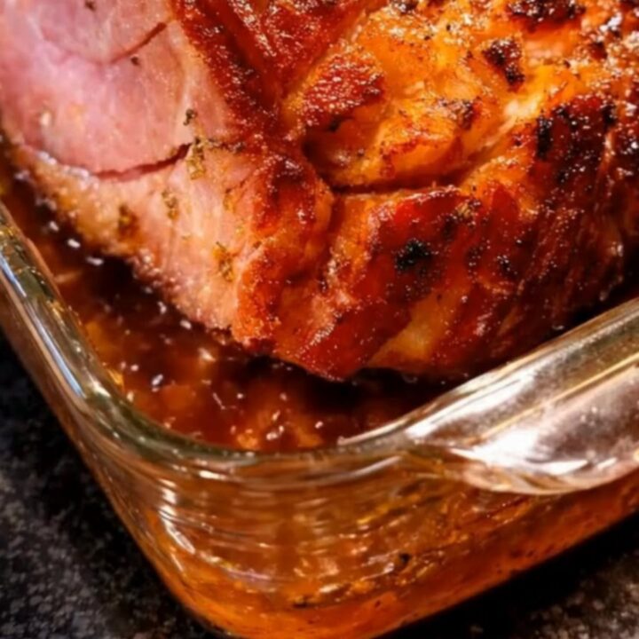 A beautifully glazed, golden-brown honey baked ham sitting in a glass dish on a rustic kitchen counter.