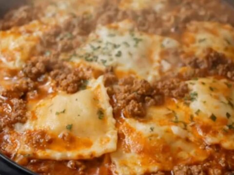 A steaming portion of ravioli lasagna being lifted from a slow cooker with a spatula, showing strings of melted cheese.