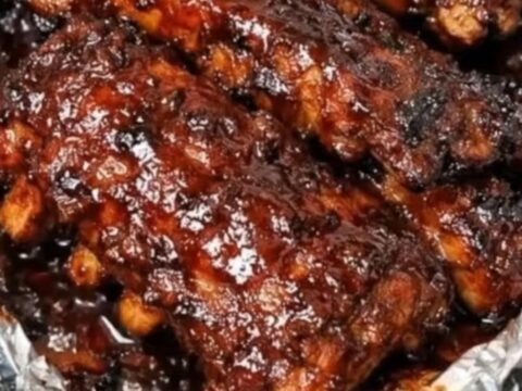 A close-up view of tender BBQ ribs being lifted with tongs from a slow cooker.