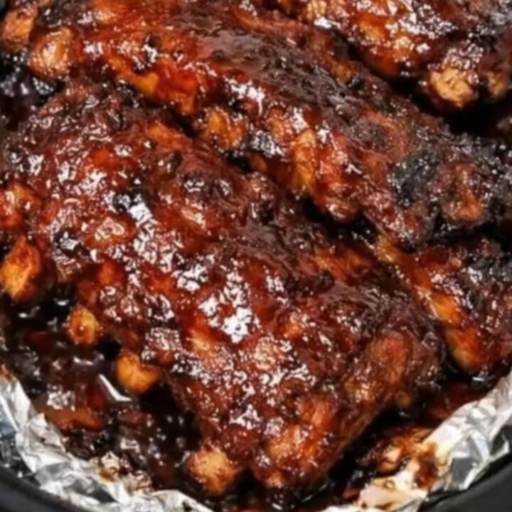 A close-up view of tender BBQ ribs being lifted with tongs from a slow cooker.