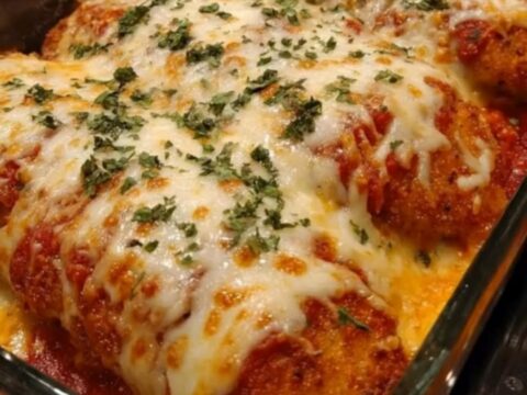 A golden, crispy chicken parmesan with bubbly, melted mozzarella cheese and a fresh parsley garnish in a glass baking dish.