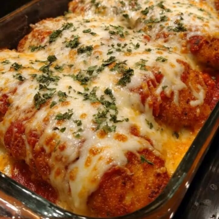 A golden, crispy chicken parmesan with bubbly, melted mozzarella cheese and a fresh parsley garnish in a glass baking dish.