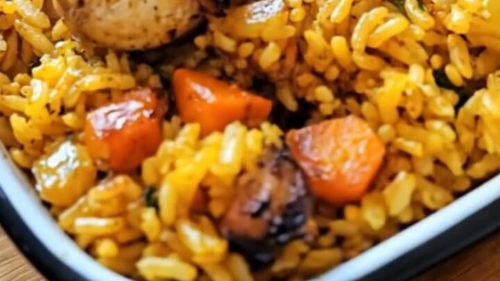 A golden roasted chicken thigh resting on a bed of fluffy yellow rice with carrots in a white ceramic dish.
