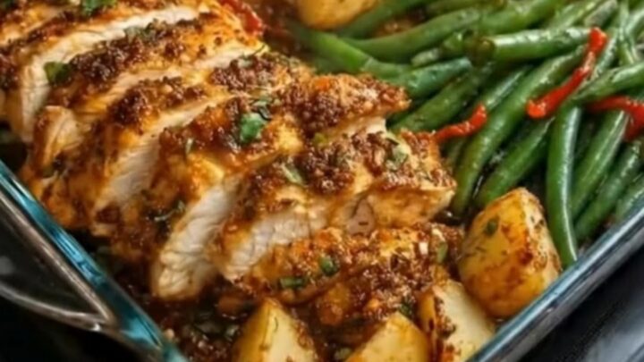 A glass baking dish filled with roasted chicken slices, golden potatoes, and bright green beans.