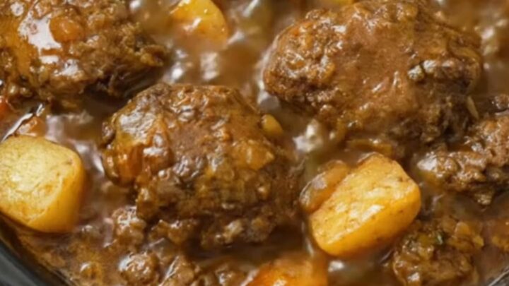 A steaming bowl of meatball stew with tender potato chunks and thick brown gravy.