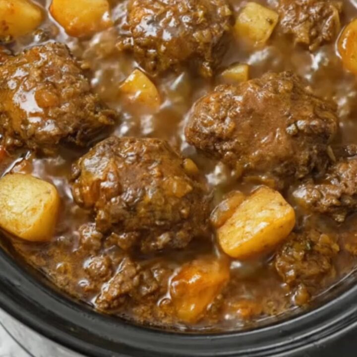 A steaming bowl of meatball stew with tender potato chunks and thick brown gravy.