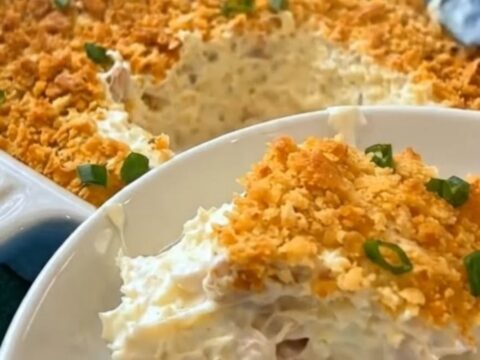 A white baking dish filled with bubbling Million Dollar Chicken Casserole topped with a golden-brown cracker crust and fresh