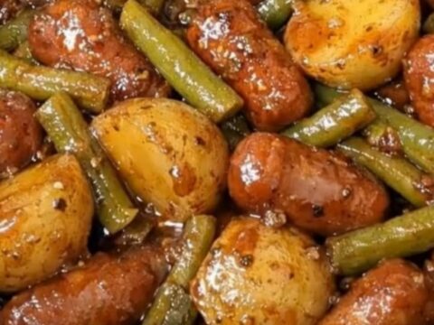 A steaming plate of honey-glazed cocktail sausages, baby potatoes, and green beans.