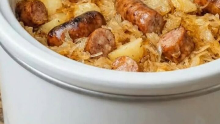 A steaming portion of sliced smoked kielbasa, tender potatoes, and sauerkraut on a white plate.